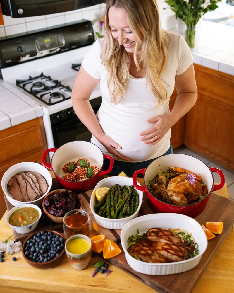 Clare Ramirez pregnant in her kitchen preparing postpartum recovery stews and meals in Dutch ovens