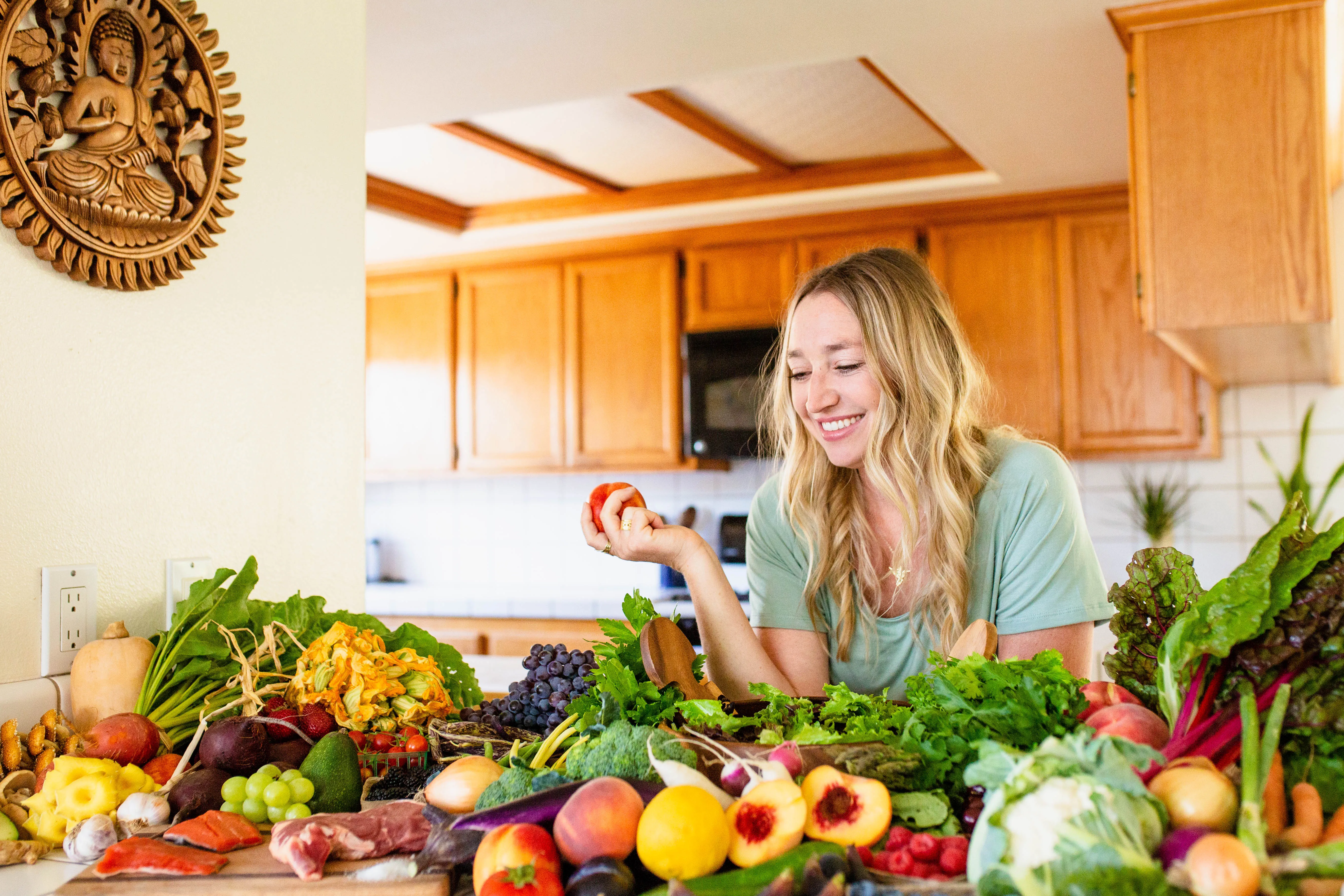 Clare Ramirez smiling in her kitchen with a fresh whole-food harvest spread