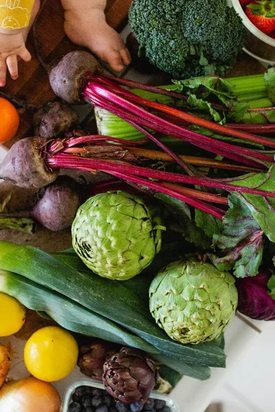 Baby toes and hands with fresh market beets, artichokes, and whole rainbow produce